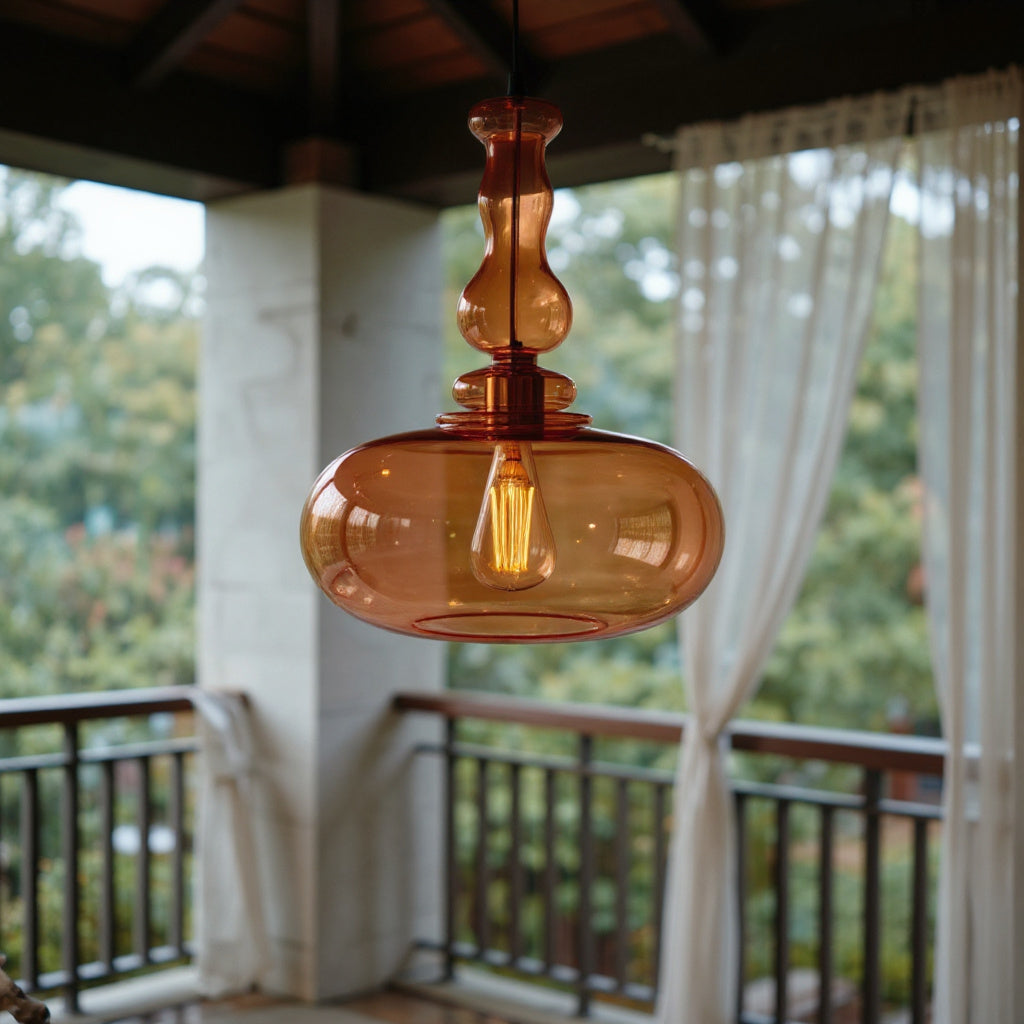 Amber glass pendant light hanging in a room with a blurred background of greenery and curtains.